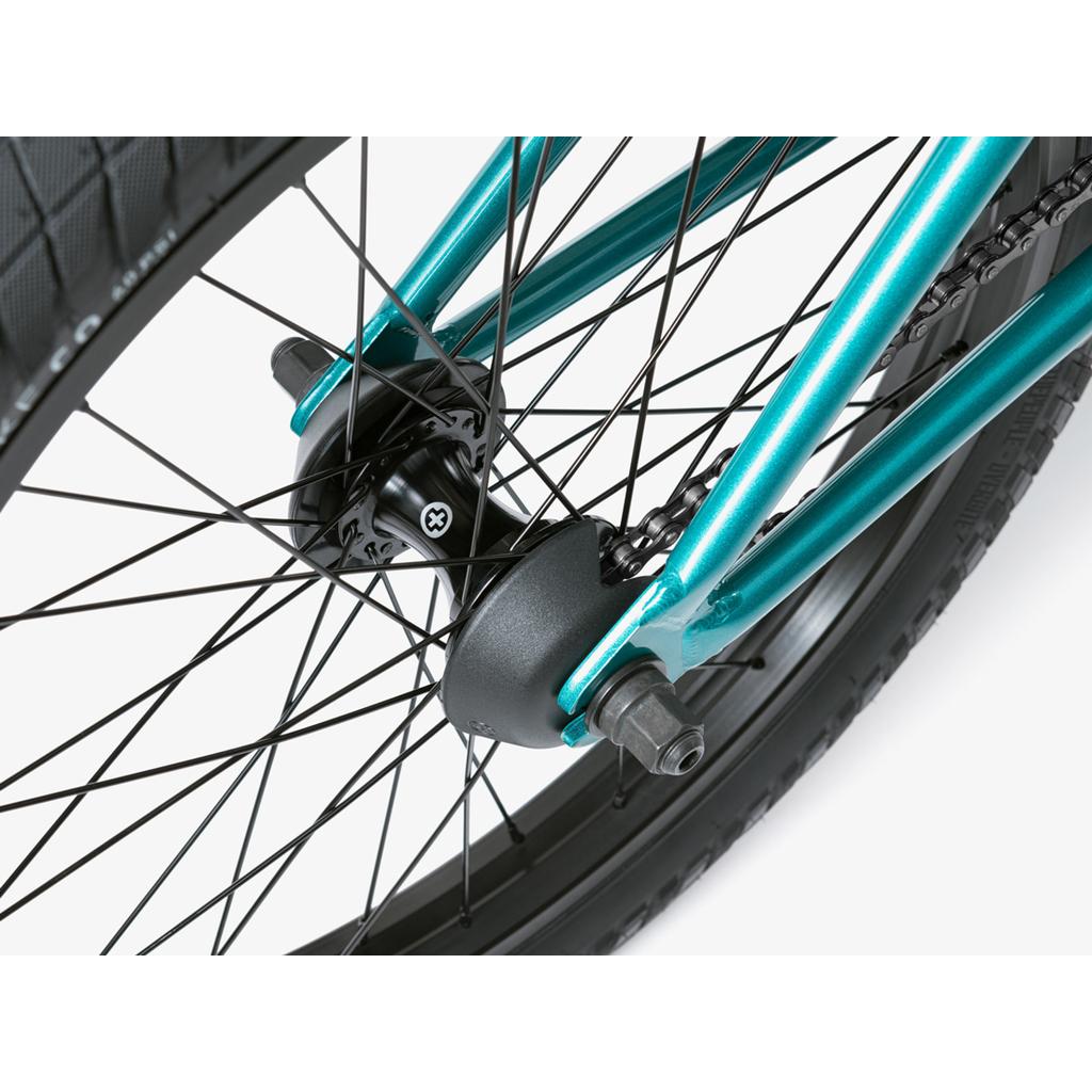 Close-up of a Wethepeople Crysis 20 Inch BMX Bike’s rear wheel, highlighting black spokes, teal frame, axle, chain segment, and Overbite Tyres.