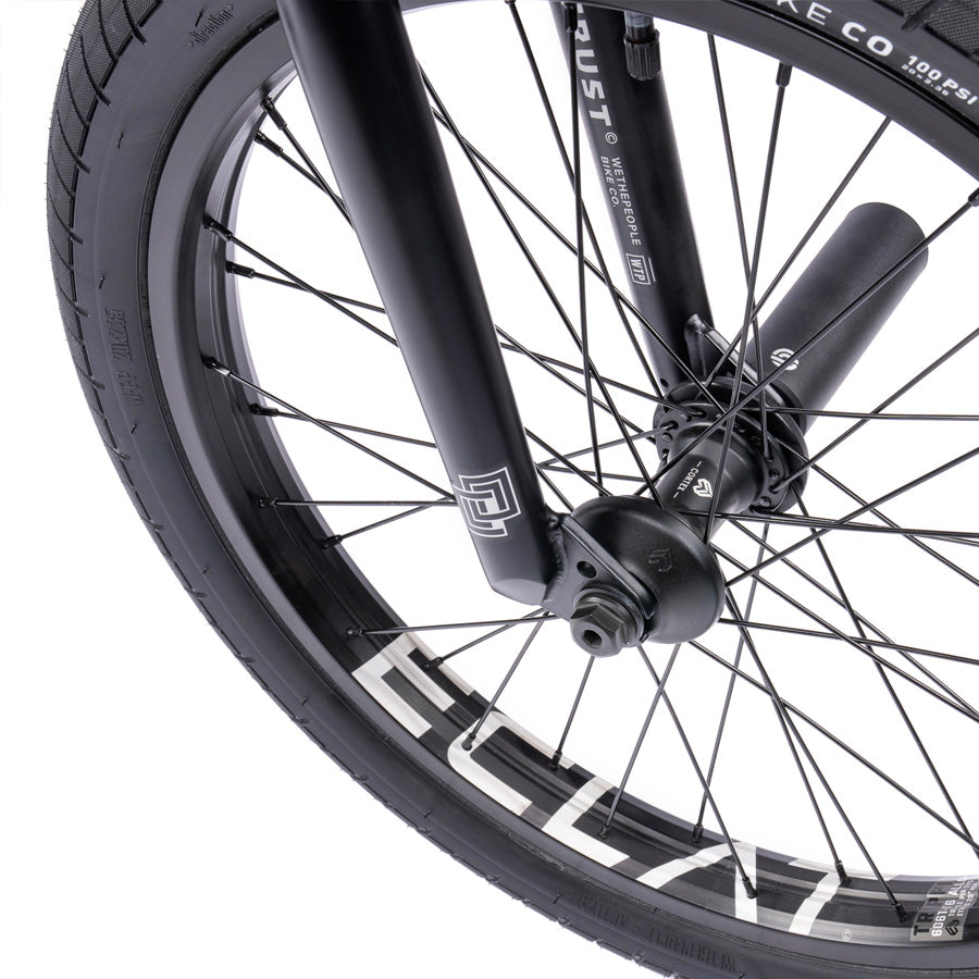 A close up of a black BMX wheel with white spokes featuring the Wethepeople Trust 20 Inch Cassette Bike.
