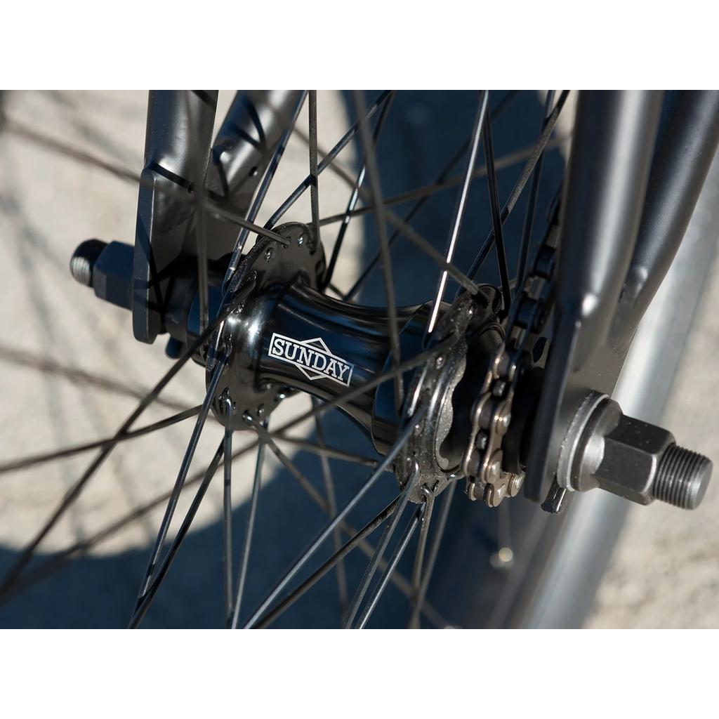 Close-up of a Sunday Scout 20 Inch Bike (2022) wheel hub, displaying the "Sunday" branding, spokes, axle bolts, and chain—highlighting quality sealed hubs and premium aftermarket bike parts.