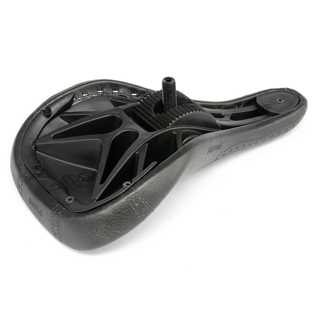 A black Eclat Exile Pivotal Seat / Tyson is pictured upside down, displaying its plastic underside and central mounting bolt—distinctive features of this BMX seat.