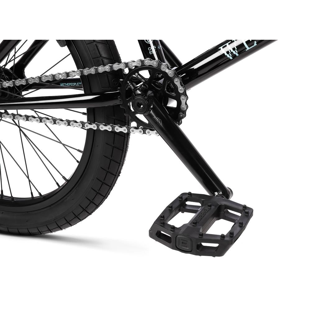 Close-up of the black BMX drivetrain on a Wethepeople Arcade 20 Inch Bike, showing the chain, sprocket, crank arm, and plastic pedal.