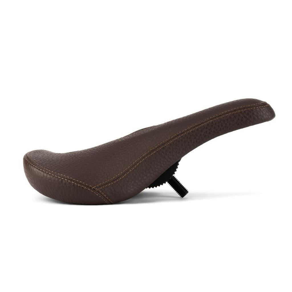 Eclat Exile Pivotal Seat: A brown leather BMX bike seat with visible stitching, shown in profile view against a white background. Designed for ergonomic comfort, it features an underside mounting bolt for easy installation.