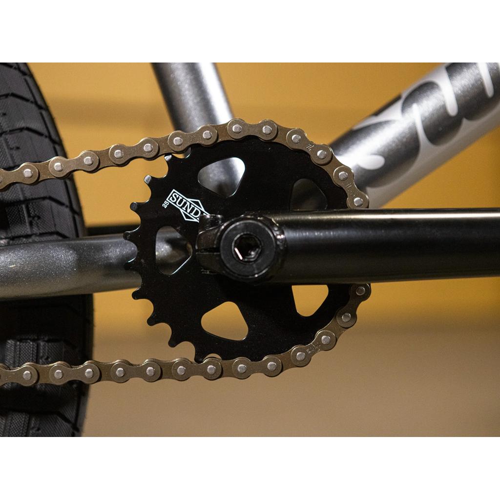 Close-up of a bicycle crankset showing a black "Sunday" chainring, chain, pedal arm, and rear tire—featuring Odyssey parts for reliable performance on your Sunday Scout 20 Inch Bike.
