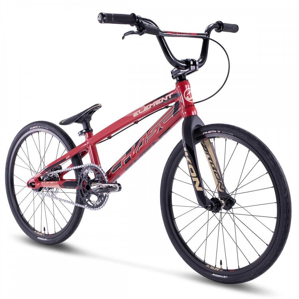 The Chase Element Expert Bike features a red BMX frame with black handlebars, seat, and tires. The Expert XL frame boasts distinctive graphics and a brand logo. It is equipped with Ikon carbon forks for front suspension and has a single gear system.