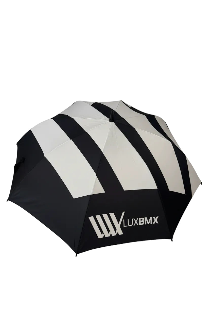 The LUXBMX Race Track Umbrella is black and white with diagonal stripes, a carbon pole, double-stitched seams, and the "LUXBMX" logo on one panel.
