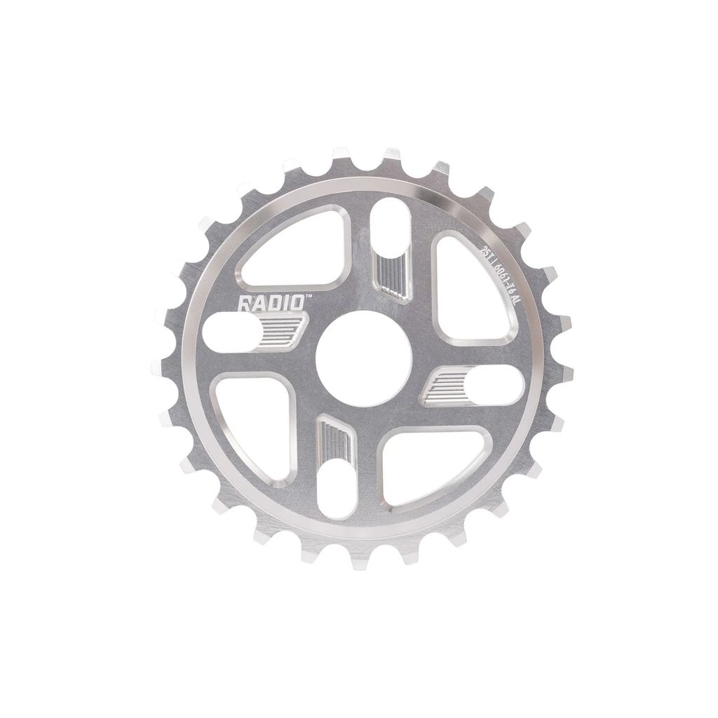 The Radio Axis Sprocket is a silver bicycle chainring with 26 teeth and cutouts, expertly CNC machined from sturdy 6061-T6 alloy, featuring the "RADIO" brand name engraved on its surface.