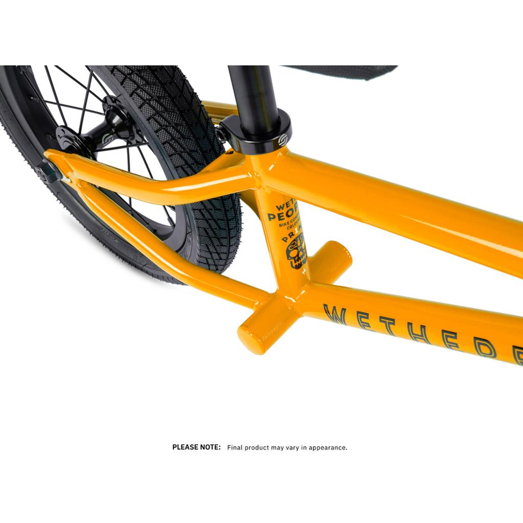 Close-up of a yellow Wethepeople Prime 12 Inch Balance Bike frame with black BMX tires, showing brand logos and details. Text below reads: "PLEASE NOTE: Final product may vary in appearance.