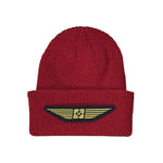 The Fit Bike Co Gold Wing Cuffed Beanie is red, crafted from hypoallergenic acrylic with a folded brim, and adorned with a distinctive yellow and black patch featuring wings and a star.