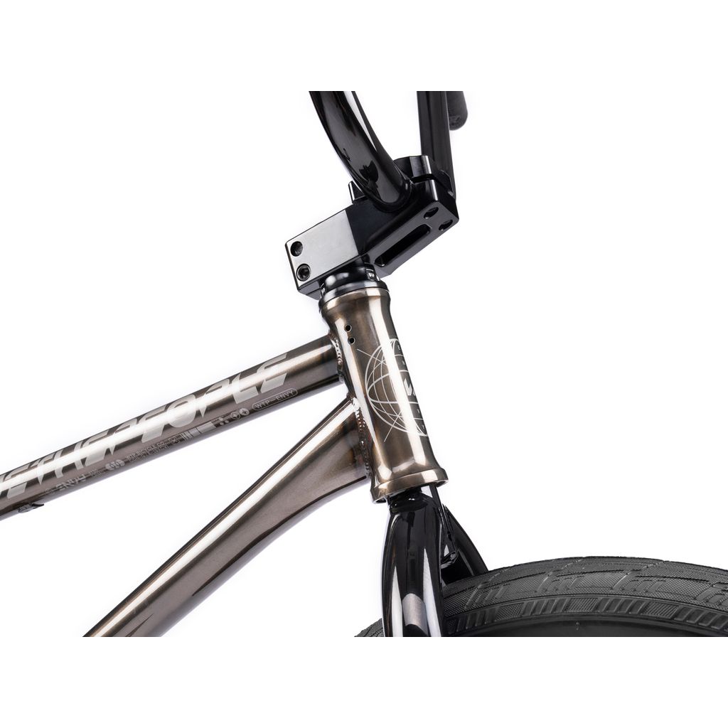 Close-up of the Wethepeople Envy 20 Inch Bike frame highlights the handlebars, front tire, and branded frame junction. This BMX masterpiece boasts a metallic finish, geometric logo, and Eclat Tibia Cranks for peak performance.