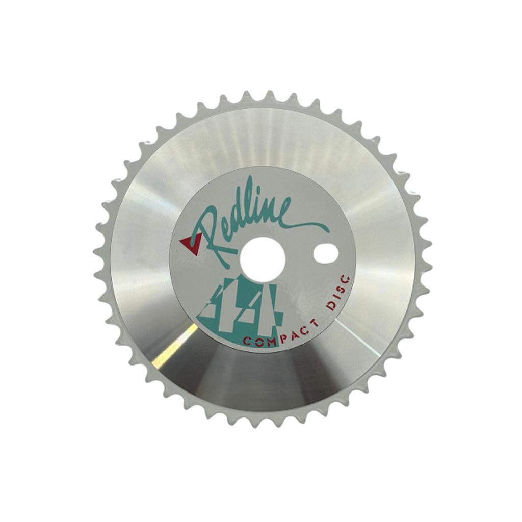 The Redline By Kastan Power Disc Front Sprocket is a circular metallic chainring with 44 teeth, CNC machined from 6061 alloy and labeled "Redline 44T Compact Disc" in green and red on a reflective silver finish.