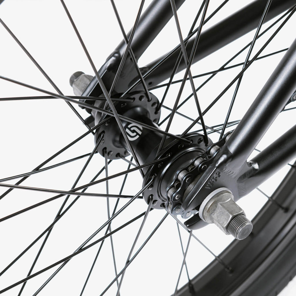 A close up of a black BMX wheel with spokes featuring the Wethepeople CRS 20 Inch Bike and Eclat Surge Pedals.