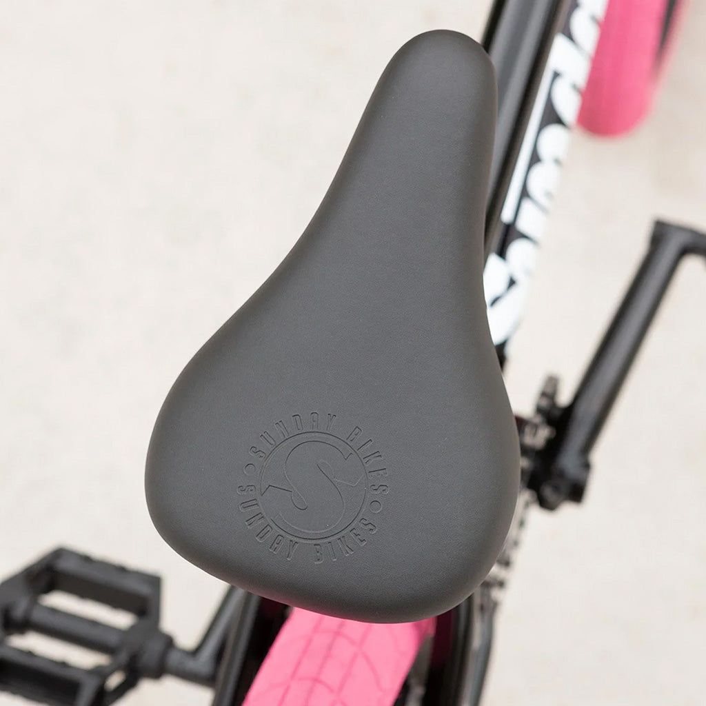 A close up of the seat of a black bike with pink rims, showcasing the Sunday Blueprint 20 inch Bike.