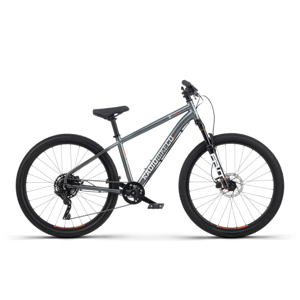 A grey Radio 26 Inch Zuma Sus Bike, featuring thick tires, a suspension fork, disc brakes, and a black saddle. This lightweight kid-sized MTB is displayed on a white background.