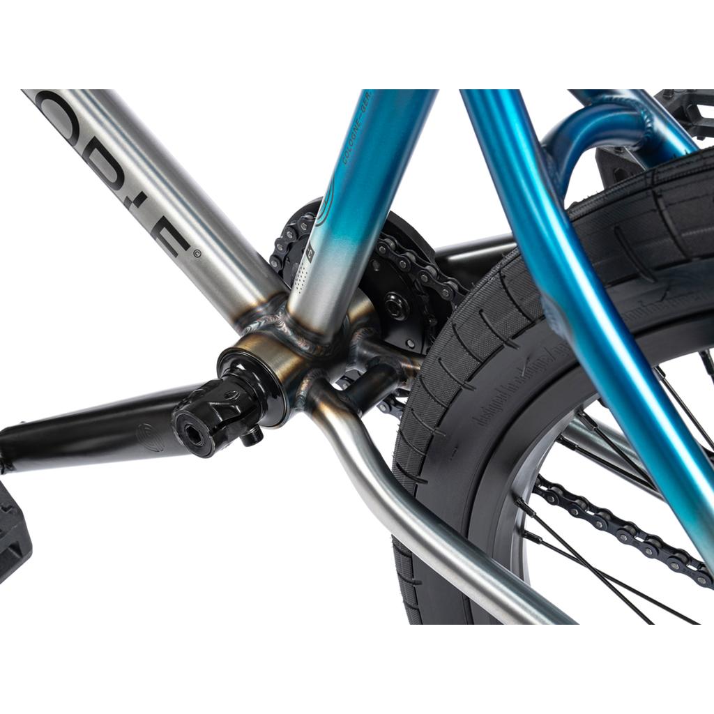 Close-up view of the Wethepeople Reason Shift 20 Inch Bike’s rear frame featuring full chromoly chain, cog, tire, and pedal in a blue and silver color scheme.