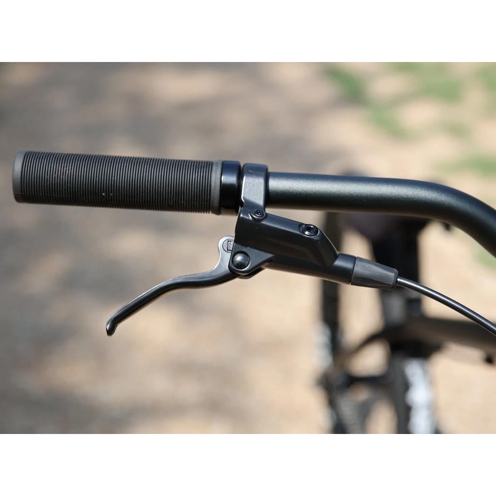 Close-up of the Fairdale Hareraiser FX 26 Inch Bike's handlebar featuring a black rubber grip and brake lever on a 4130 chromoly frame, photographed outdoors against a blurred background.