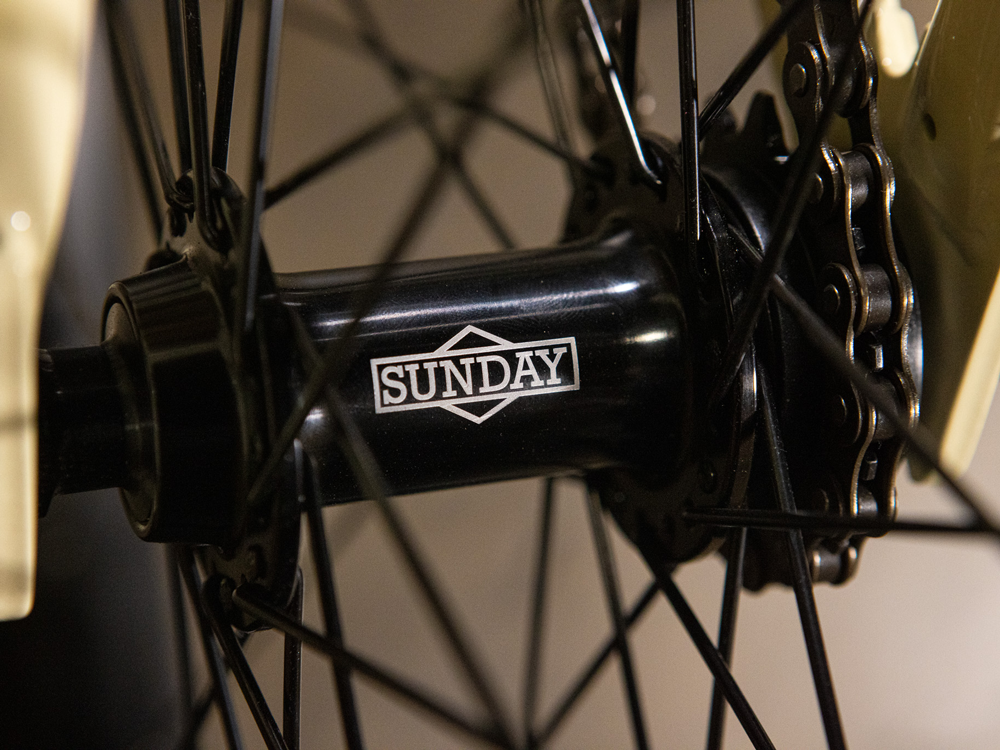 Close-up of a bicycle wheel hub with black spokes and "SUNDAY" printed in white on the hub, highlighting the quality and sleek design featured on the Sunday High C 29 Inch Bike.