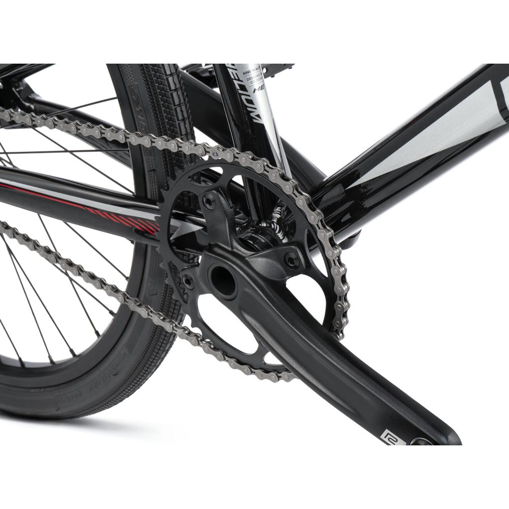 Close-up of the black crankset, chainring, and chain on the Radio Helium Pro 24 Inch Cruiser Bike, with part of the rear wheel and frame visible.