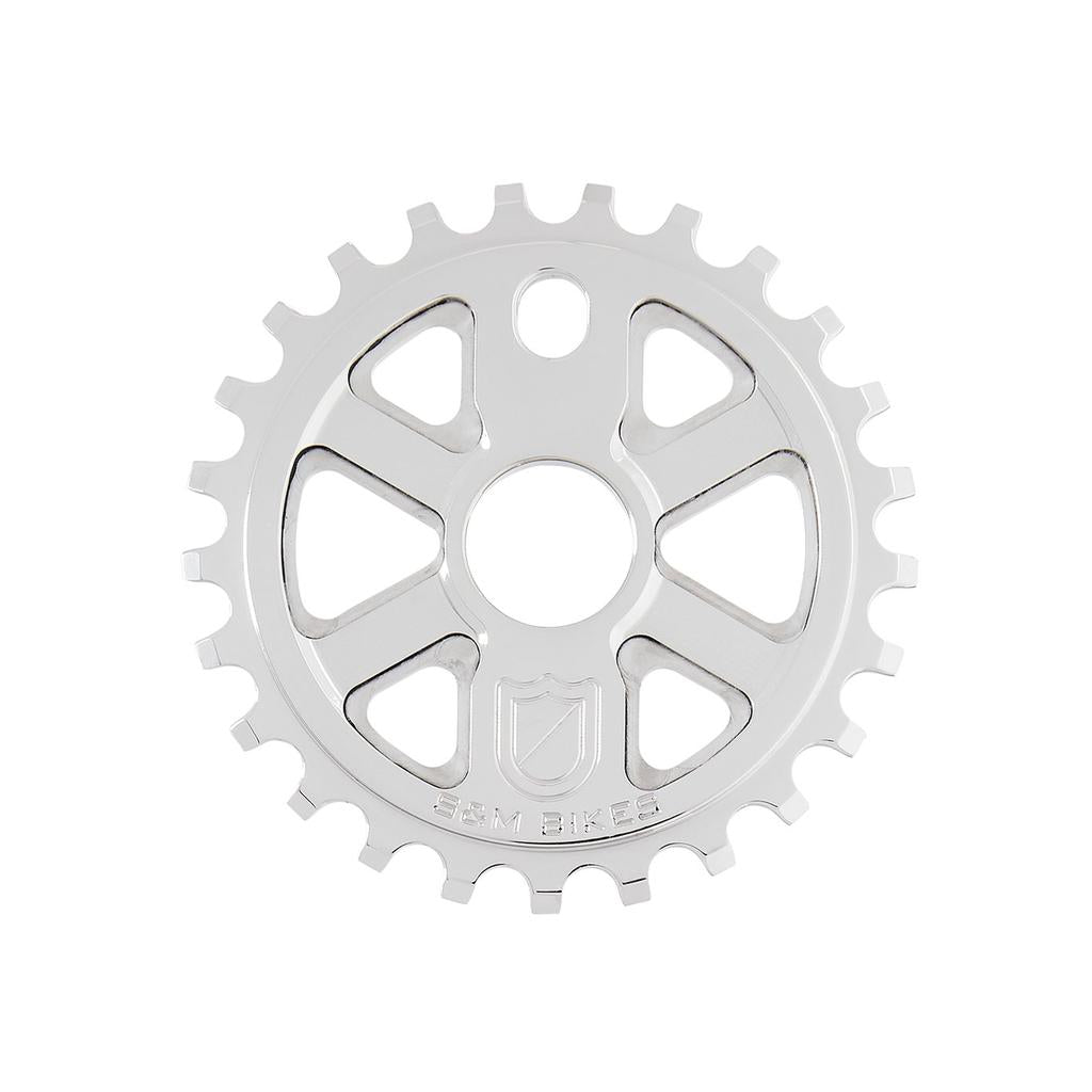 The S&M X-Man Sprocket is a silver CNC-machined 7075 T6 aluminum bicycle sprocket with a circular center hole, cut-out triangles, 1/8″ teeth, and "S&M BIKES" engraved at the bottom. Made in the USA.