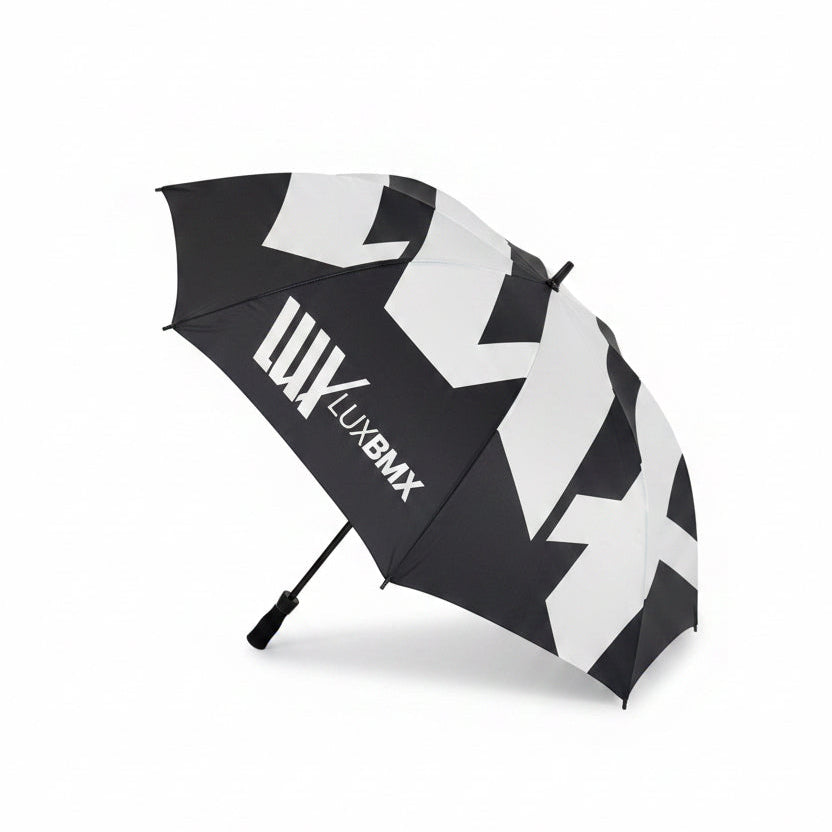 The LUXBMX Race Track Umbrella is black with bold white geometric patterns, double-stitched seams, and "LUXBMX" printed on one panel, shown against a plain white background.