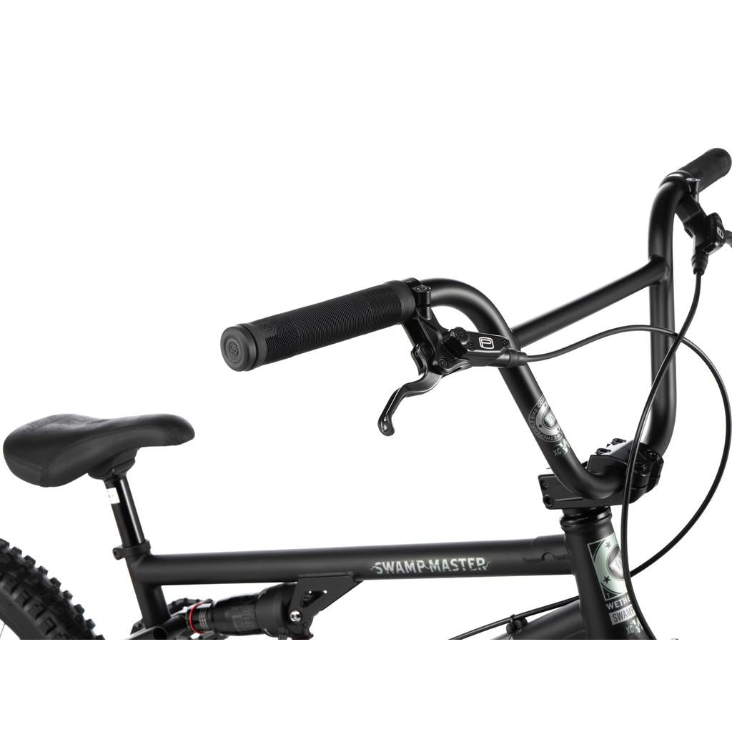 Close-up view of the Wethepeople Swampmaster 20 Inch Bike, featuring black BMX MTB fusion handlebars, grips, brake levers, and a rear suspension shock.