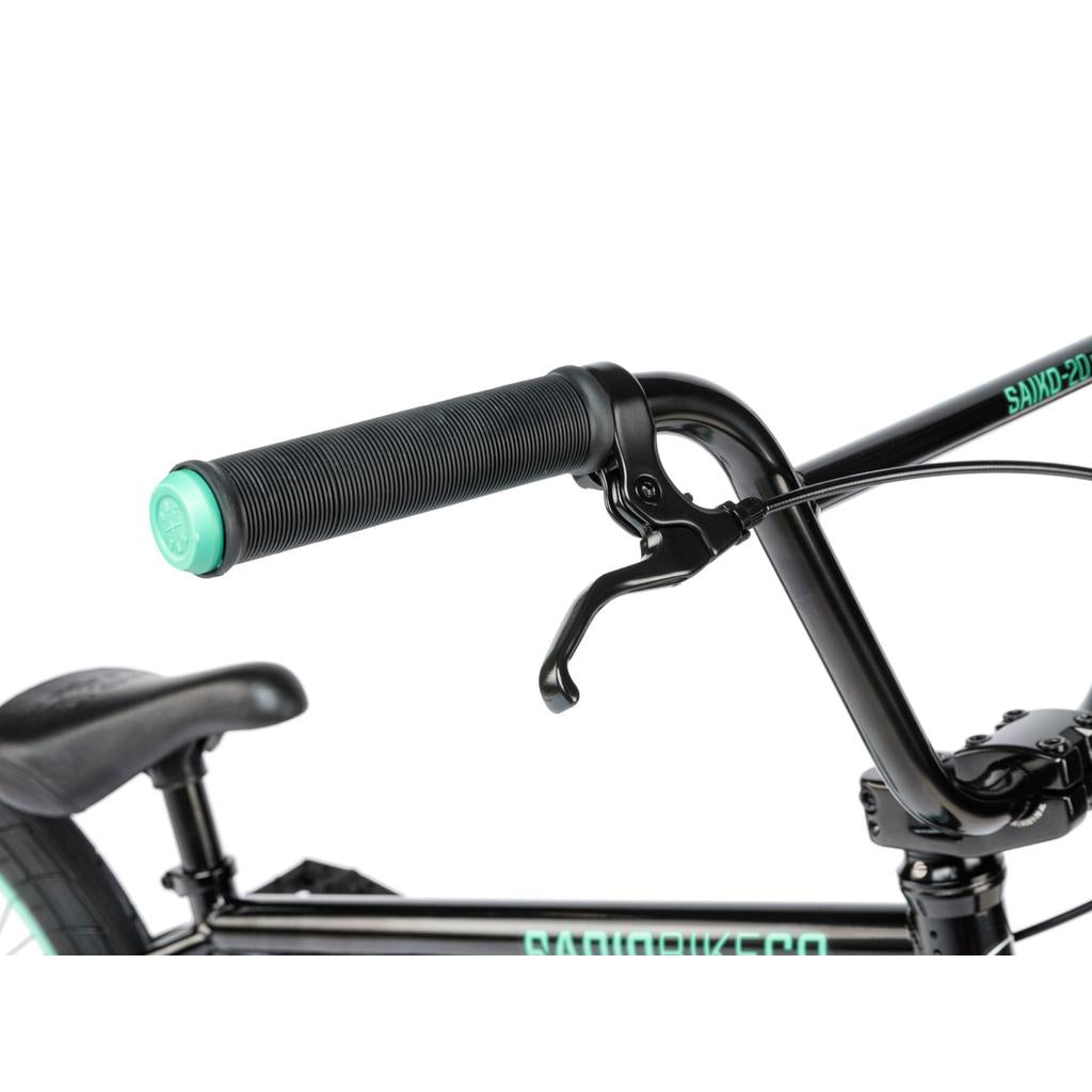 Close-up of the Radio Saiko 20 Inch Bike's handlebar with mint green end cap, brake lever, Salt Tracer Tyres, seat, and part of the frame. This sleek kids BMX is shown against a white background.