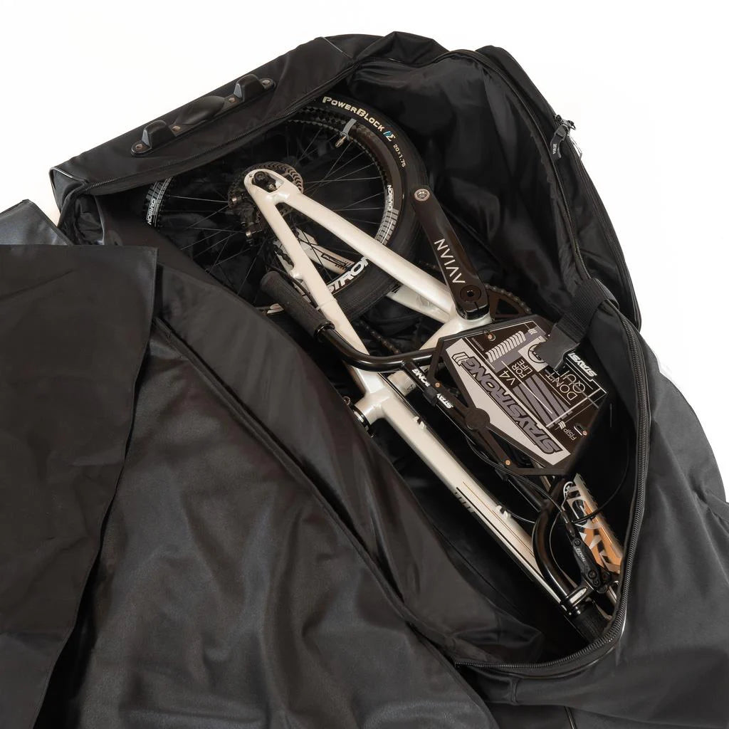 A bicycle is disassembled and packed inside a partially unzipped Stay Strong Bike Carry Bag V2, revealing the bike components and frame.