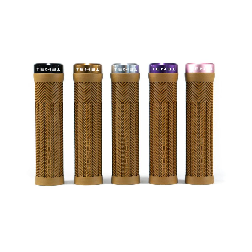 Five Tenet Components Icon Grips in tan with a textured finish and extra soft rubber stand upright in a row on a white background. Each mountain bike grip features a differently colored lock-on end cap—black, gold, silver, purple, and pink—for added style and ensures a secure fit while delivering superior comfort on every ride.