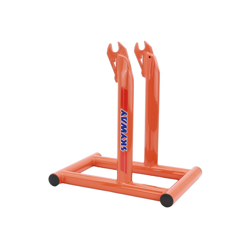 The Skyway Stolz Stand is an orange metal BMX bike stand with two upright prongs, a rectangular base, and "SKYWAY" on the side—perfect for displaying your classic ride or Skyway TA Replica.