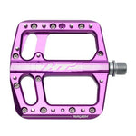 The HT Components ANS12 Raven Pedals are purple aluminum mountain bike pedals with multiple grip pins and two large cutouts, shown from the side with the spindle visible on the right.