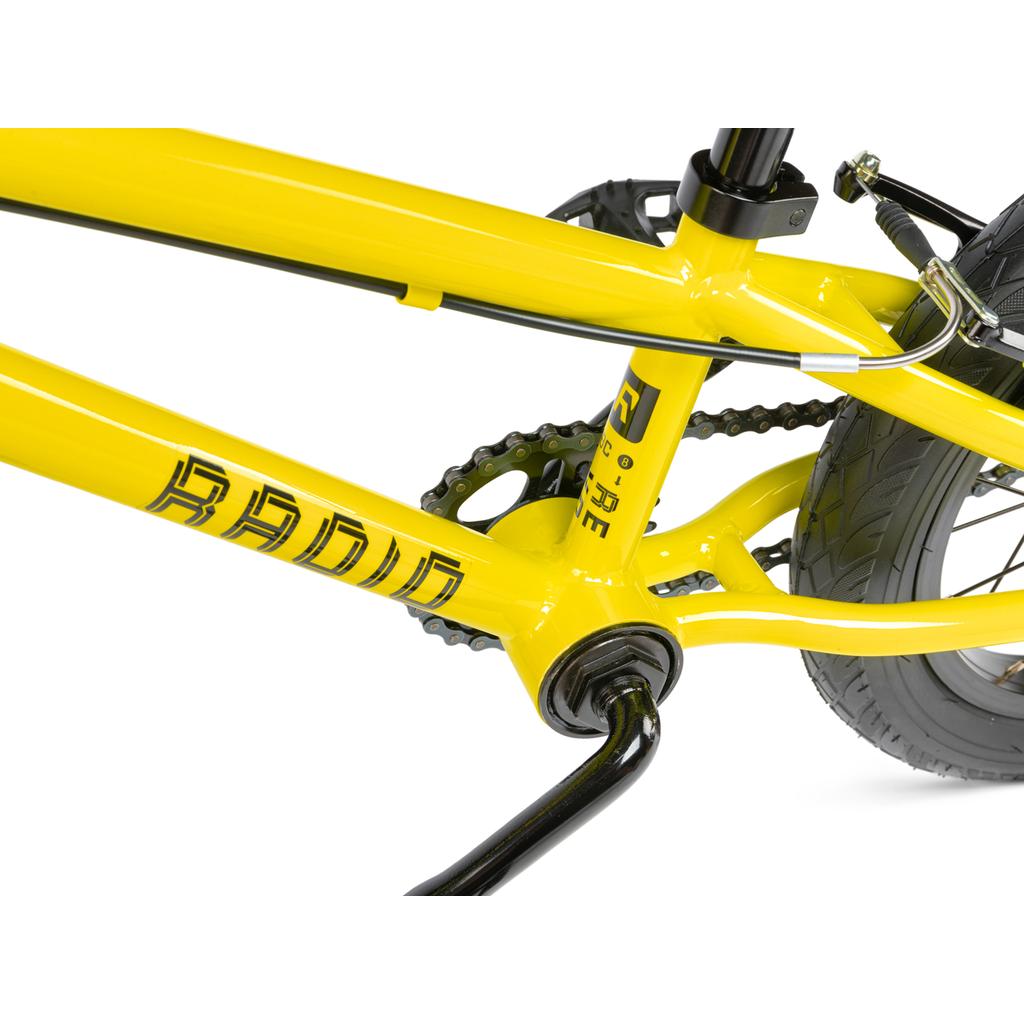 Close-up of the Radio Revo 14 Inch bike’s yellow frame, highlighting the crank, chain, rear tire, and part of the pedal arm—an ideal choice for a first bike.