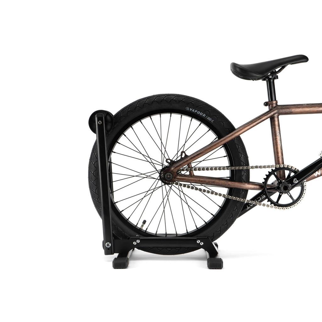 A 6MIL BS-01 Bike Stand supports a bicycle's rear wheel, displaying the chain, seat, and frame against a white background.