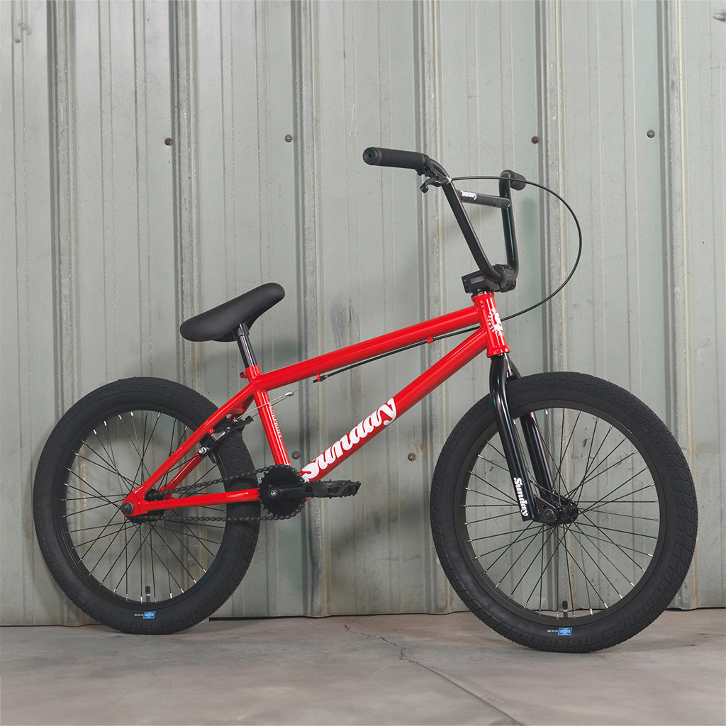 A red Sunday Blueprint 20 inch Bike leaning against a wall, perfect for beginners.