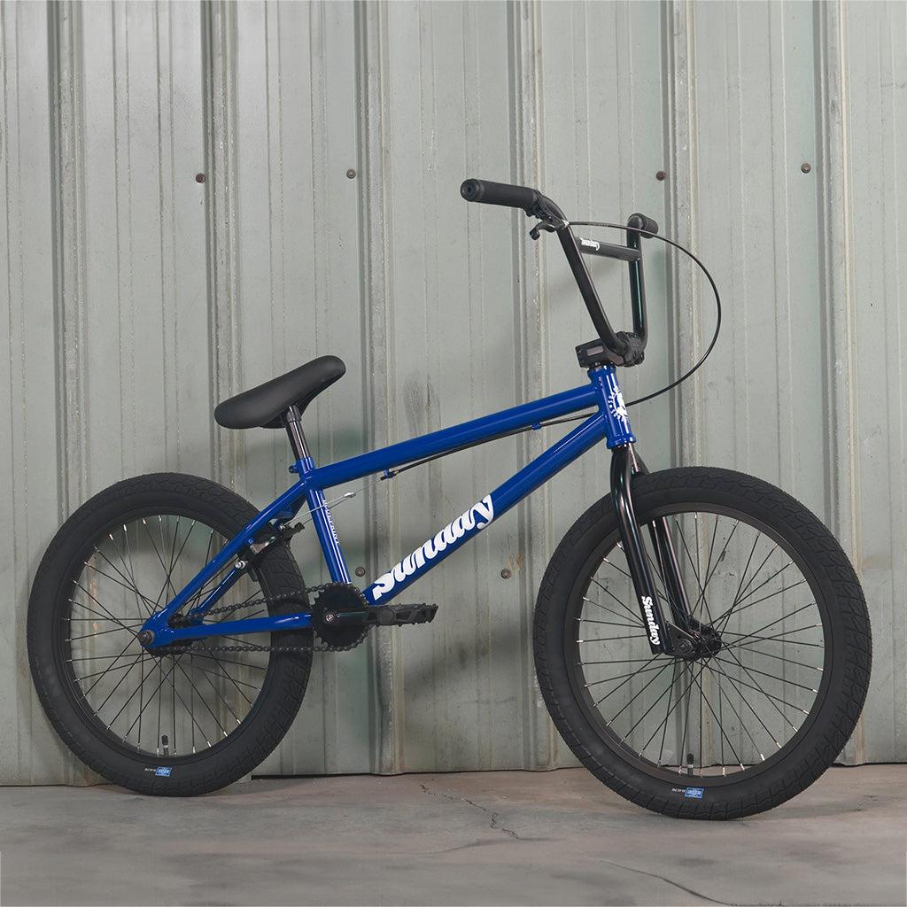 A blue Sunday Blueprint 20 inch bike leaning against a wall.