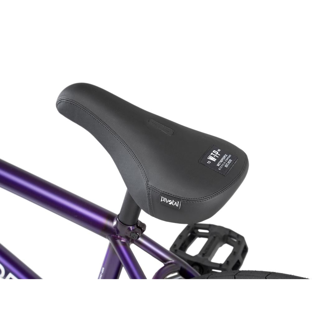 Close-up of a black bicycle seat on the Wethepeople Reason Shift 20 Inch Bike's purple frame, showing the label and textured surface.