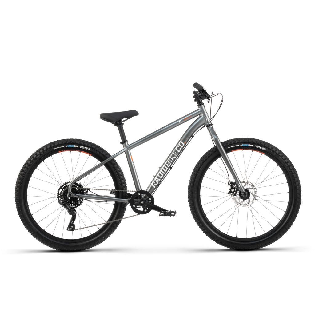 A silver Radio 26 Inch Zuma Bike with a lightweight alloy frame, large knobby tires, a black seat, and disc brakes. The kid-sized MTB features a front suspension fork and is labeled "MOTO-BICICCO.