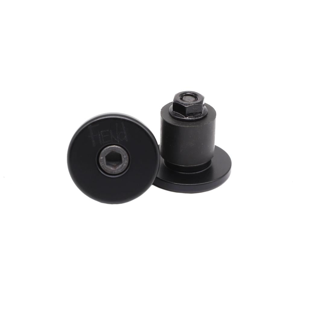 The Fiend Alloy Bar Ends, shown here in black, are pictured with one standing upright and the other laying flat—each featuring a central hex bolt. These alloy plugs are designed to protect your bike and offer a secure, stylish finish for your handlebars.