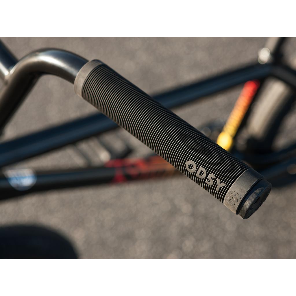 Close-up of a textured black ODI handlebar grip on the Sunday Sound Wave Special 20 Inch Bike (2023), with part of its Chromoly BMX frame and pavement visible in the background.