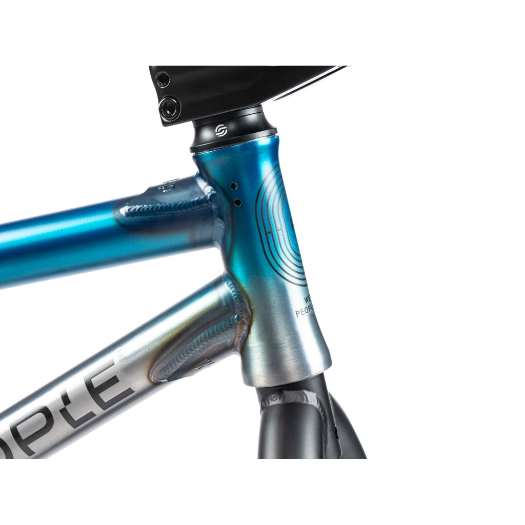 Close-up of the Wethepeople Reason Shift 20 Inch Bike's head tube and top tube junction, with a blue-silver gradient finish, full chromoly frame, and part of its circular logo.
