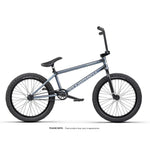 The Wethepeople Revolver 20 Inch Bike is shown in profile on a white background, with a metallic blue frame, black saddle, handlebars, pedals, and tires, featuring high-end components for top performance.