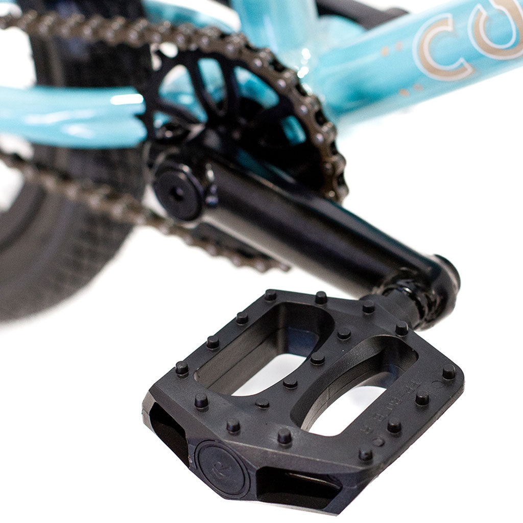 Close-up of a black bicycle pedal attached to a crank arm, with parts of the chain and teal Colony Horizon 14" Micro Freestyle Bike lightweight alloy frame visible in the background.