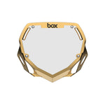 The Box TWO Number Plate / Small Gold Chrome features an angular design, "box" logo at the top, and four mounting holes—ideal for BMX riders who want to stand out on the track.