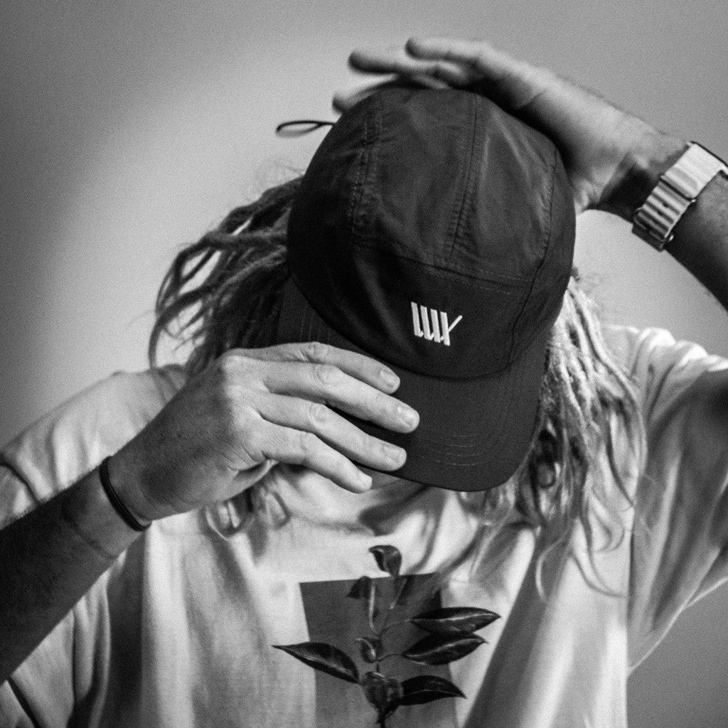 A black and white photo of a man with dreadlocks wearing a LUXBMX Aero 5 Panel Cap - Black.