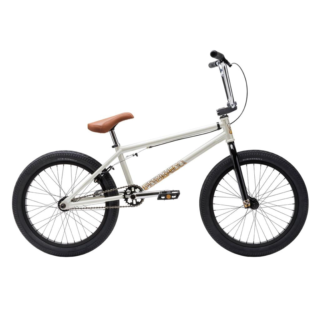 The Fit Bike Co Series One Bike features a white Cro-Mo frame, brown seat, black handlebars and wheels, and gold branding on the frame, shown in a side view on a white background.