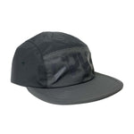 The Cult Runner Cap is a dark gray, low-profile hat made from recycled nylon, featuring a prominent stylized black logo across the front panel and a flat brim.