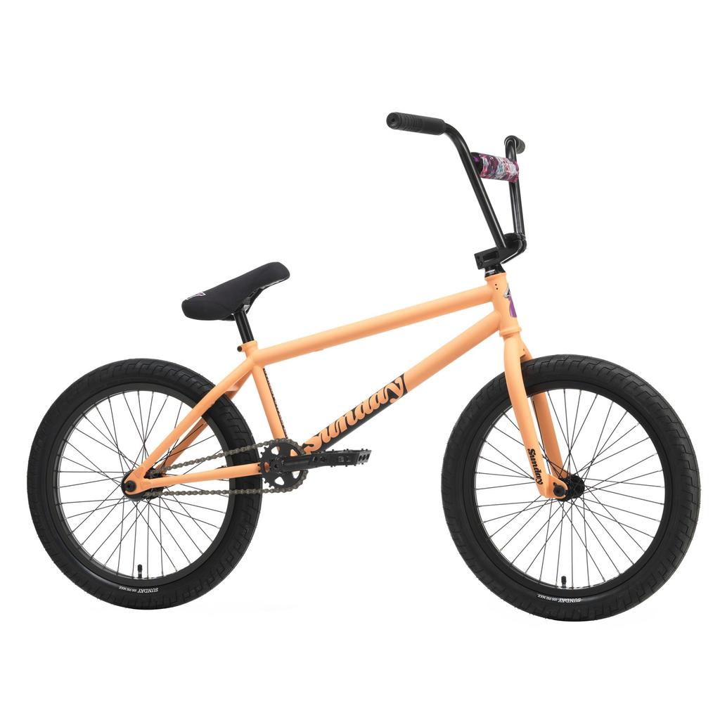The Sunday Street Sweeper 20 Inch Bike features a matte orange chromoly frame, black handlebars, seat, and wheels, with a "Sunday" logo on the frame and patterned handlebar pad—Jake Seeley signature style.