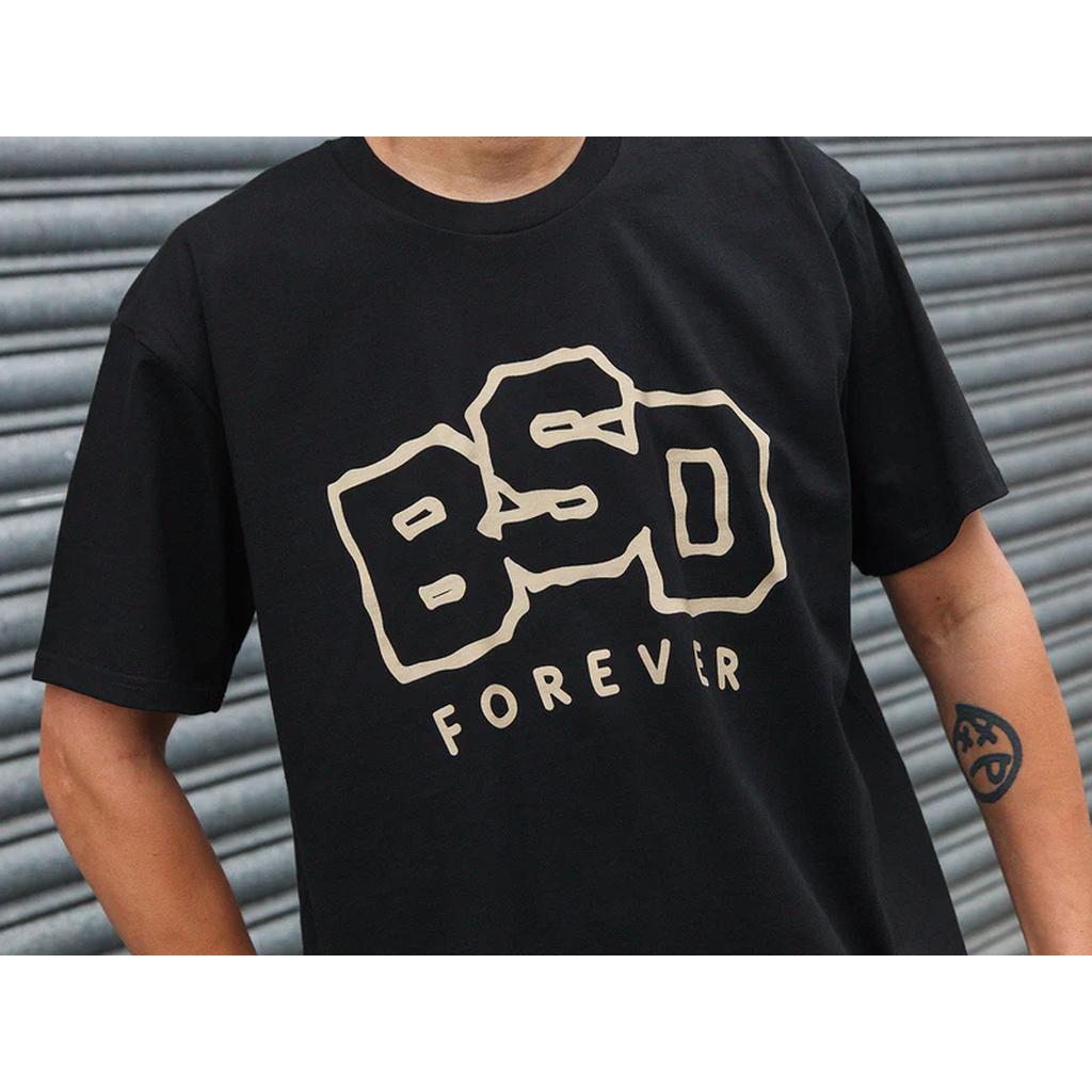 Person wearing a BSD Wobbler T-Shirt in black with "BSD FOREVER" in bold cream letters, standing in front of a metal shutter.