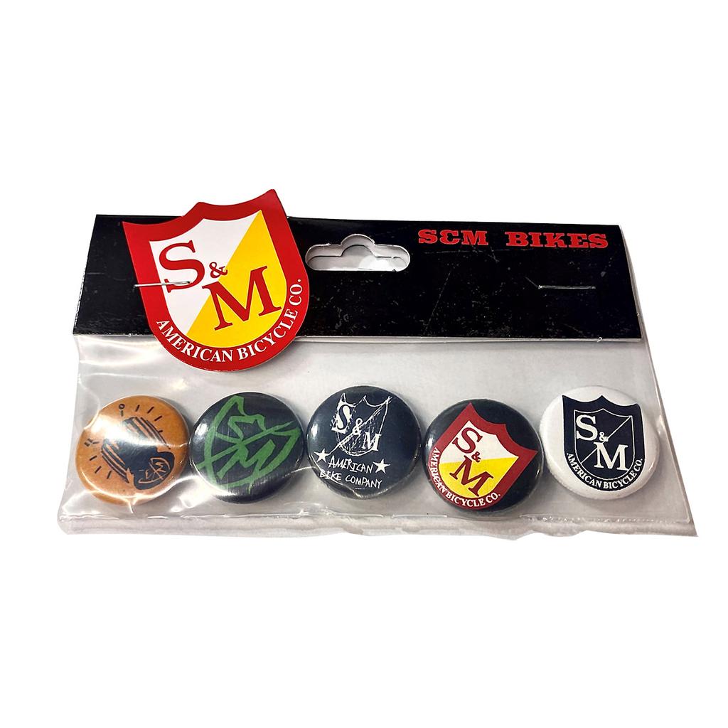 The S&M Pin Back Button Pack contains five unique logo buttons from the American Bicycle Co., stylishly packaged with a branded cardboard header in a clear plastic bag, ideal for any cycling enthusiast's collection.