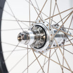 Close-up of a bicycle wheel hub with metal spokes arranged radially, showcasing the axle, bearings, and gear cog in detail—featuring titanium spokes from the ION BMX C20 Carbon Titanium V1.5 Planetary 20 Inch Wheelset.