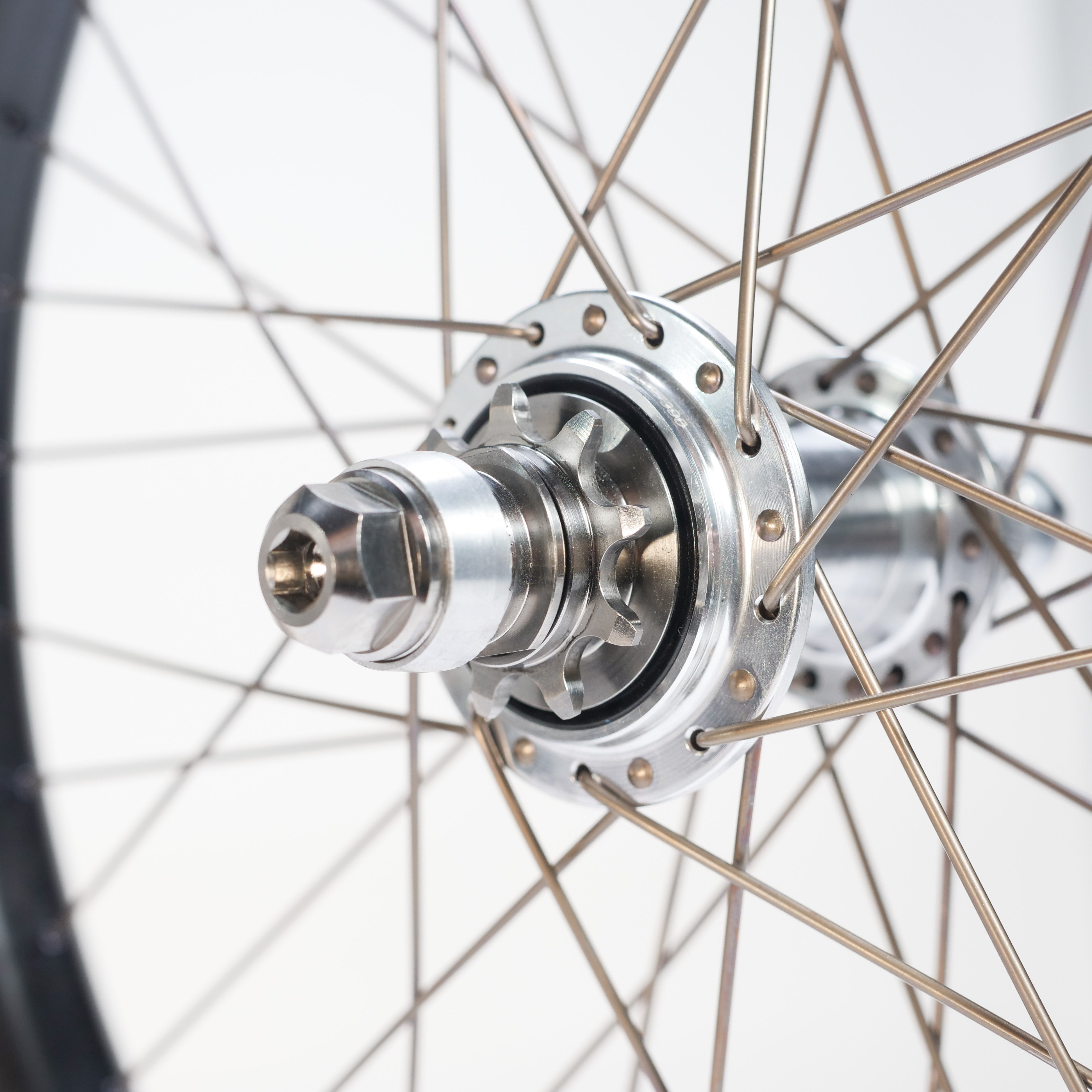 Close-up of a bicycle wheel hub with metal spokes arranged radially, showcasing the axle, bearings, and gear cog in detail—featuring titanium spokes from the ION BMX C20 Carbon Titanium V1.5 Planetary 20 Inch Wheelset.