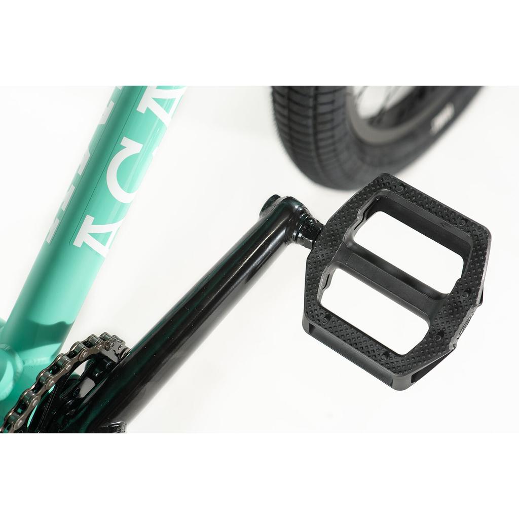 Close-up of a black pedal and crank arm on an Academy Trooper 20 Inch Bike with a teal beginner BMX frame, showing part of the rear tire in the background.
